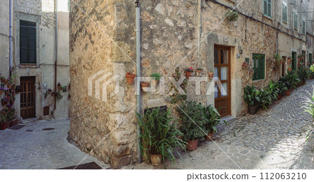 Charming Cobblestone Street with Rustic Potted Plants in Mediterranean Village Charming Cobblestone Street with Rustic Potted Plants in Mediterranean Village 112063210