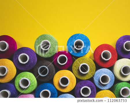 Multicolored threads for sewing and embroidery on yellow background 112063733