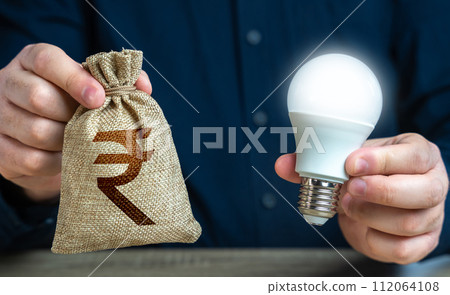 Indian rupee money bag and burning idea light bulb in the hands of a man. Offering financial incentives to enhancing energy efficiency. Reduce carbon footprint. Investment in an idea. 112064108