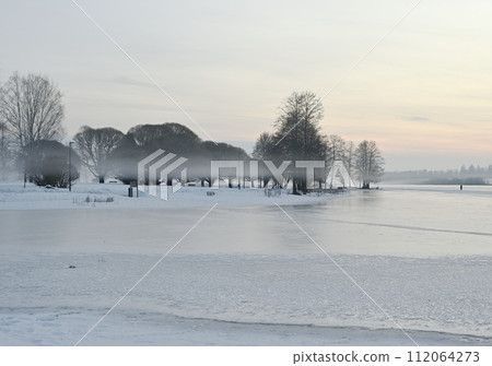 Tranquil frozen lake with misty treeline 112064273