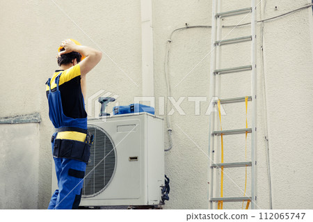 Certified engineer contracted to repair external air conditioner starting work shift. Expert technician wearing protective gear preparing to fix broken outdoor hvac system Certified engineer contracted to repair external air conditioner starting work shift. Expert technician wearing protective gear preparing to fix broken outdoor hvac system 112065747