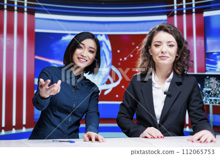 Journalists team discuss daily news, presenting latest events on international television program in newsroom. Two women broadcasters working on entertainment segment with reportage. 112065753