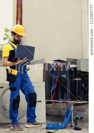 Certified expert commissioned for outside air conditioner routine check up, imputing data on laptop. Trained mechanic doing hvac system safety check, looking for defective internal parts Certified expert commissioned for outside air conditioner routine check up, imputing data on laptop. Trained mechanic doing hvac system safety check, looking for defective internal parts 112065777