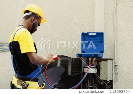 Proficient african american worker doing routine condenser maintenance, assembling manifold indicators before starting work. Qualified electrician getting equipment ready to check freon leaks Proficient african american worker doing routine condenser maintenance, assembling manifold indicators before starting work. Qualified electrician getting equipment ready to check freon leaks 112065794