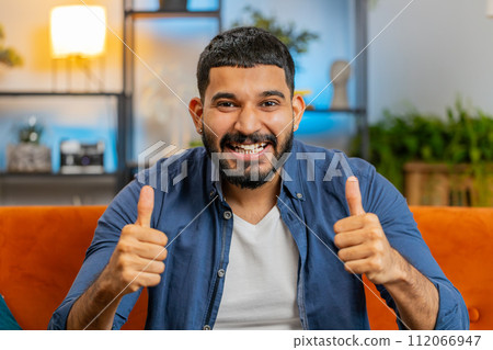 Happy Indian young man watching TV celebrating success winning good news lottery game luck victory 112066947