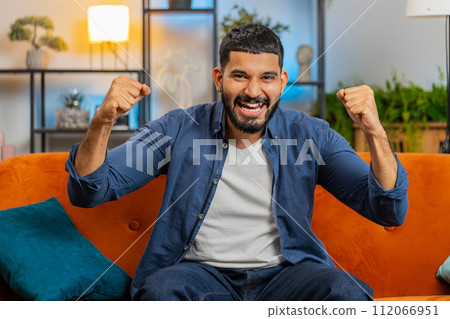 Happy Indian young man watching TV celebrating success winning good news lottery game luck victory 112066951