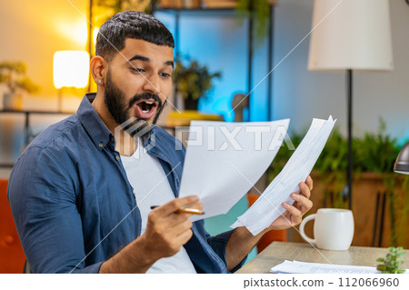 Indian man freelancer working with documents from home office analyzing reading business report 112066960