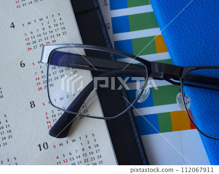 桌上放置的圖表、眼鏡、日曆和筆記本 112067911