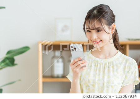 A woman who operates a smartphone in the living room. 112067934