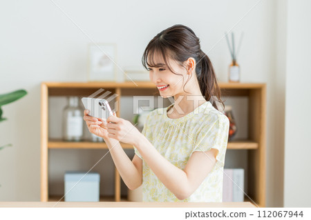 A woman who operates a smartphone in the living room. 112067944