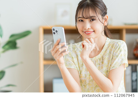 A woman who operates a smartphone in the living room. 112067945