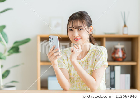 A woman who operates a smartphone in the living room. 112067946