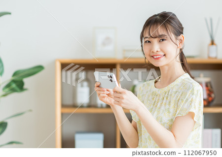 A woman who operates a smartphone in the living room. 112067950