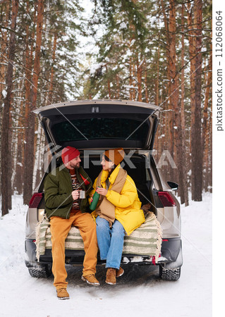 Young Caucasian couple sitting in car trunk drinking tea and talking on cold winter day Young Caucasian couple sitting in car trunk drinking tea and talking on cold winter day 112068064