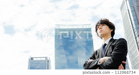 A businessman in his 30s looks off into the distance with his arms folded with a serious expression in a business district during the day A businessman in his 30s looks off into the distance with his arms folded with a serious expression in a business district during the day 112068734