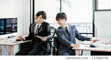 Two men working in an office with a colleague back to back, turning around and consulting while having a work meeting 112068748