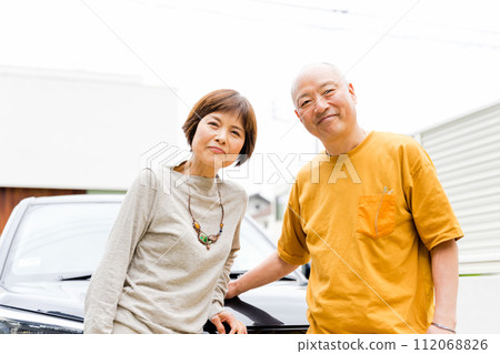 Two friendly elderly couples in their 50s and 60s looking at the camera in front of their car Two friendly elderly couples in their 50s and 60s looking at the camera in front of their car 112068826