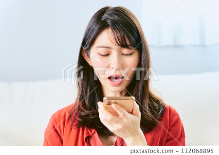A Japanese woman in her 30s uses AI voice recognition technology to speak to enter information into a smartphone inside a room. A Japanese woman in her 30s uses AI voice recognition technology to speak to enter information into a smartphone inside a room. 112068895