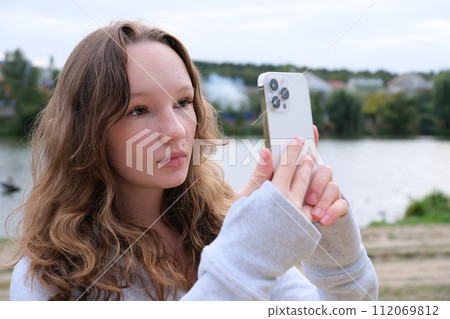 Red-haired young girl taking selfie with her smartphone against snowy background. Selective focus. High quality photo 112069812