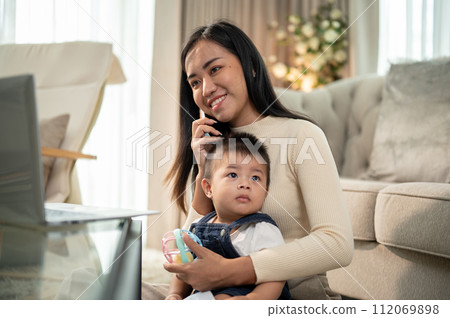 A positive Asian businesswoman mom is talking on the phone while taking care of her little son. A positive Asian businesswoman mom is talking on the phone while taking care of her little son. 112069898