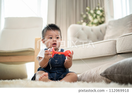 A cute, cheerful Asian baby boy is playing with toys on a carpet in the living room. 112069918