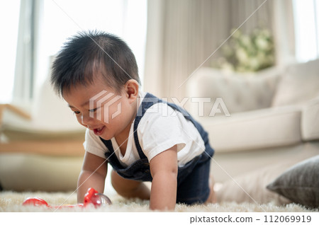A cute, cheerful Asian baby boy is playing with toys and crawling on the floor in the living room. 112069919