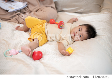 A cute, innocent Asian baby boy is playing with toys while lying on the bed in the bedroom. 112070049