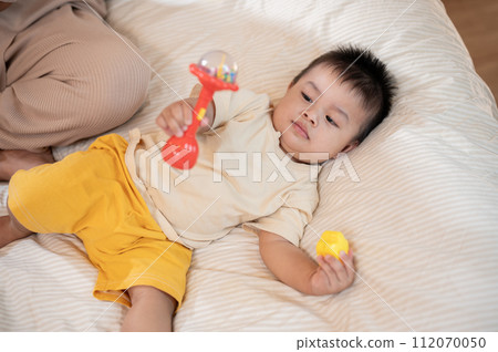 A cute, innocent Asian baby boy is playing with toys while lying on the bed in the bedroom. 112070050
