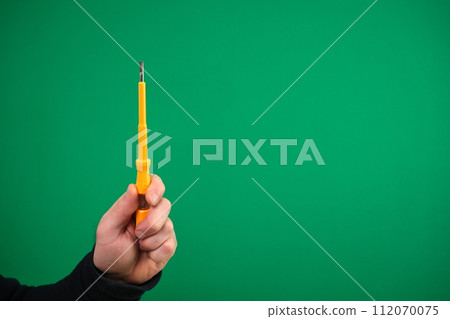 Electric yellow screwdriver with indicator in male hand on green background advertising Green background chromakey free space Electric yellow screwdriver with indicator in male hand on green background advertising Green background chromakey free space 112070075