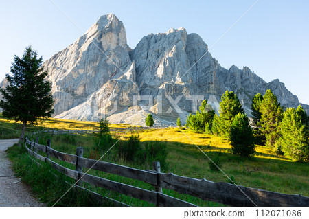 Pathway with wooden railings in alpine meadow leading to Munt de Fornella in Dolomites Pathway with wooden railings in alpine meadow leading to Munt de Fornella in Dolomites 112071086