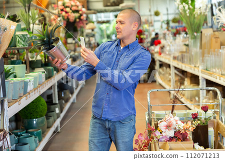 Man photographing artificial plant in home goods store Man photographing artificial plant in home goods store 112071213
