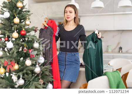 Young upset woman choosing which dress to wear 112071234
