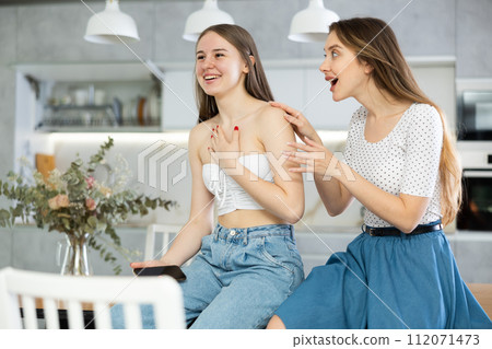 Kind middle-aged mother talking to young daughter sitting on kitchen-table 112071473