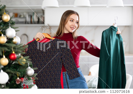 Portrait of attractive woman selecting dress for Christmas celebration 112071616