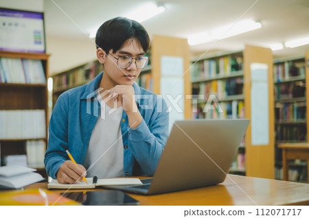 Male college students are working on laptops and searching for books to study, make reports, find useful information in college room. Concept of reading, learning and intelligence. 112071717