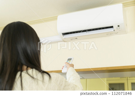 A woman operating an air conditioner (focus on the remote control) 112071846
