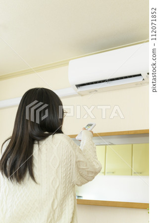 A cold woman operating an air conditioner A cold woman operating an air conditioner 112071852