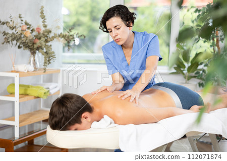 Adult woman giving back massage to young guy Adult woman giving back massage to young guy 112071874