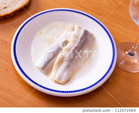 On wooden table is plate with appetizer - salted Atlantic herring fillet with pickled onions 112072069
