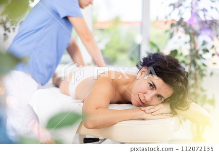 Masseur doing thigh massage to adult woman Masseur doing thigh massage to adult woman 112072135