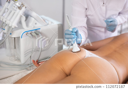 Aesthetician administering high frequency ultrasound procedure on buttocks of female patient Aesthetician administering high frequency ultrasound procedure on buttocks of female patient 112072187