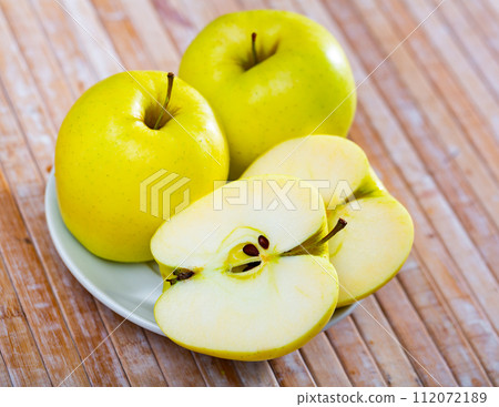 Ripe yellow whole and halved apples of golden delicious variety on table Ripe yellow whole and halved apples of golden delicious variety on table 112072189