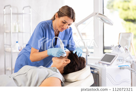 Female aesthetician administering high frequency ultrasound facial procedure on woman Female aesthetician administering high frequency ultrasound facial procedure on woman 112072321