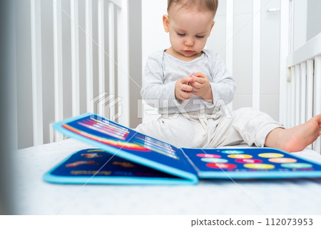 Baby playing with montessori quiet book sitting in a crib. Concept of smart books and modern educational toys Baby playing with montessori quiet book sitting in a crib. Concept of smart books and modern educational toys 112073953