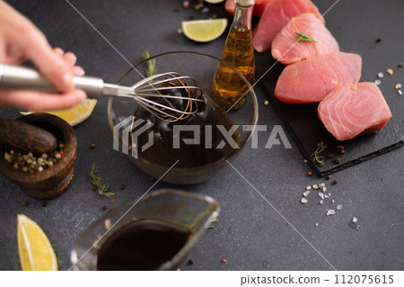 Woman mixing with whisk soy sauce and olive oil in a glass bowl making marinade to marinate Pieces of Fresh tuna Fish fillet Woman mixing with whisk soy sauce and olive oil in a glass bowl making marinade to marinate Pieces of Fresh tuna Fish fillet 112075615