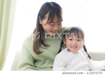 Friendly parent and child sitting on the sofa, child looking at camera 112075773