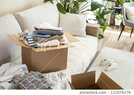 Recycling concept. A box sits on the sofa full of clothes for donation, recycling or disposal. 112076276