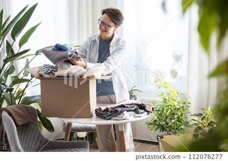 Donation concept. A woman puts clothes in a box at home for donation, recycling or disposal. 112076277