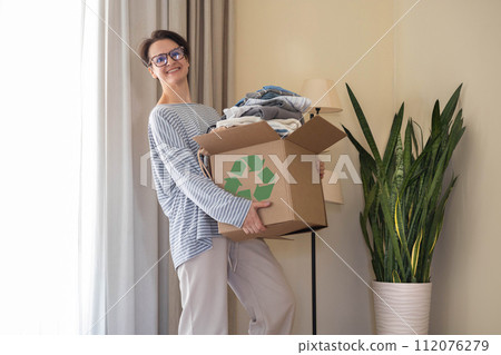 Recycling concept. A woman holds a cardboard box with clothes for recycling. Recycling concept. A woman holds a cardboard box with clothes for recycling. 112076279