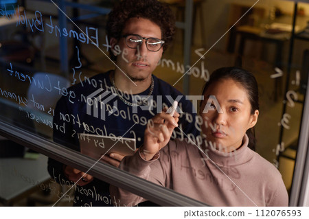 High angle of two young programmers working together on code writing it on glass wall in modern office 112076593